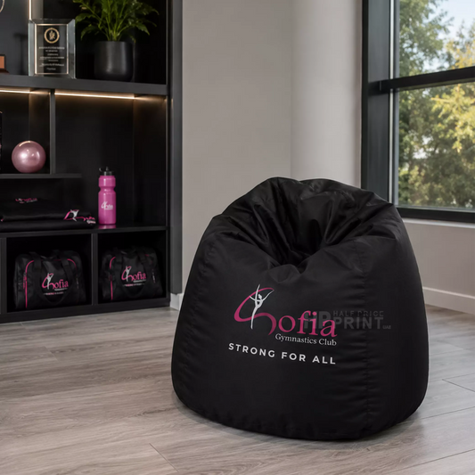 Black bean bag chair with 'Gofia Gymnastics Club' branding in a room with shelves and window.