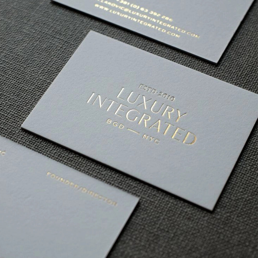 A stack of gray business cards with gold foiling text that reads 'LUXURY INTEGRATED' and other text indicating a business name and address.