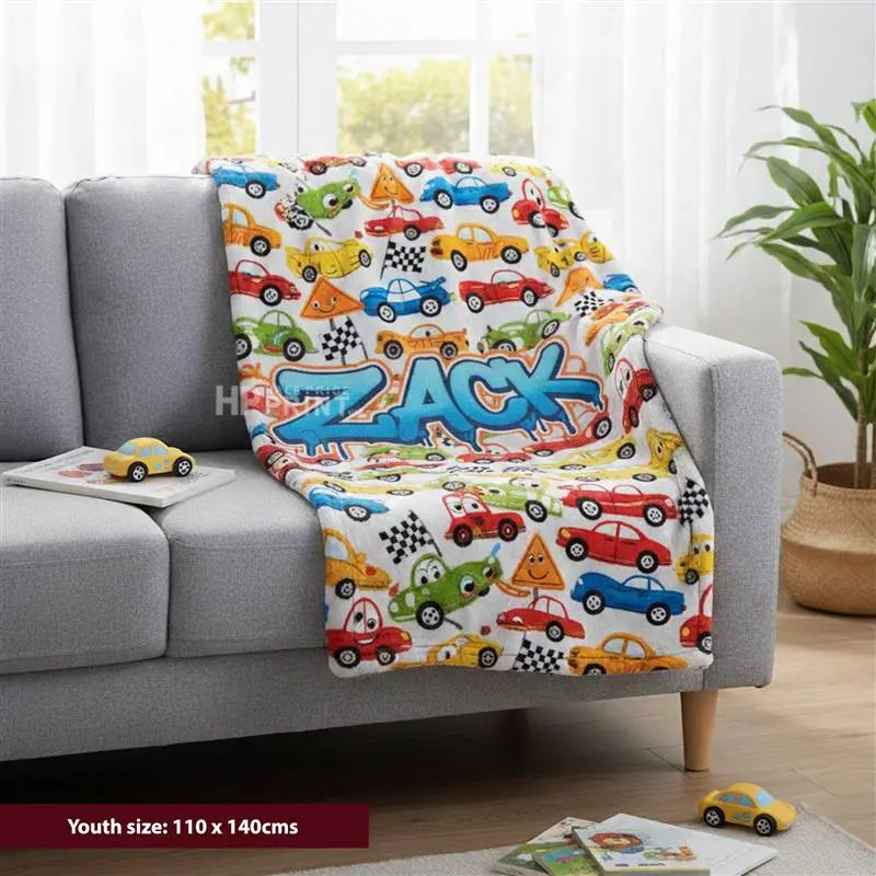 Colorful children's blanket with 'Zack' printed on a gray couch in a living room.