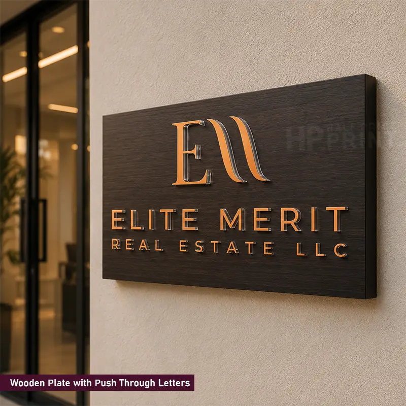 A rectangular dark wood sign mounted on a beige wall, featuring raised metallic gold letters that read 'ELITE MERIT REAL ESTATE LLC' with a stylized 'EM' logo above. A small text label at the bottom left reads 'Wooden Plate with Push Through Letters.