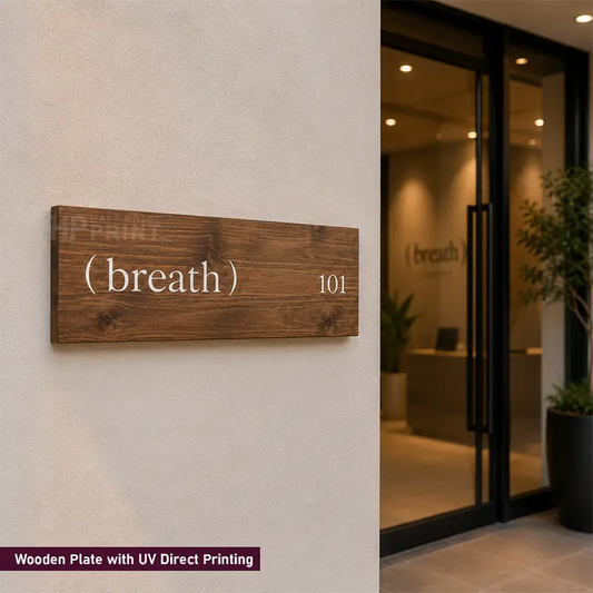 A rectangular wooden house number sign with UV direct printing, featuring the text '( breath) 101' in white on a dark brown wood grain background, mounted on a textured beige wall next to a glass door entryway.