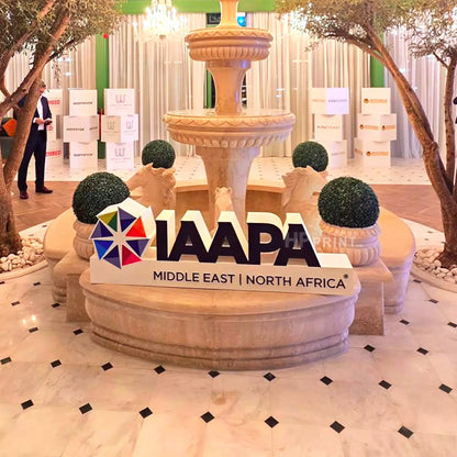 A large freestanding IAAPA Middle East | North Africa sign with the event logo, placed in front of a decorative stone fountain and small statues in an indoor event space.
