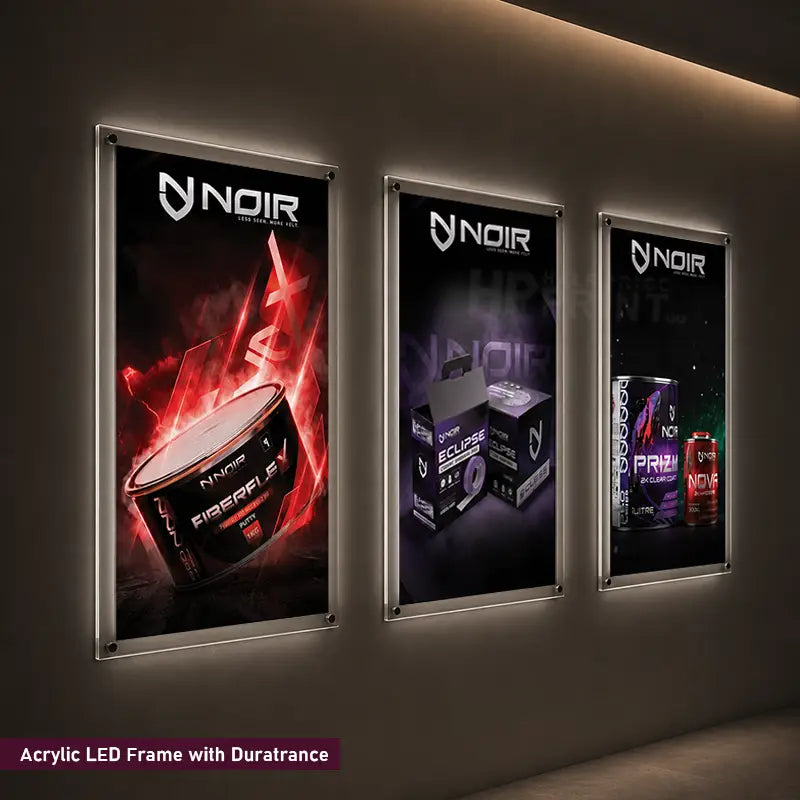 Three vertically oriented acrylic LED frame wall art displays mounted on a dark wall, each showing different branded product posters. The left panel glows red, the center panel is dark purple, and the right panel is dark with neon accents.