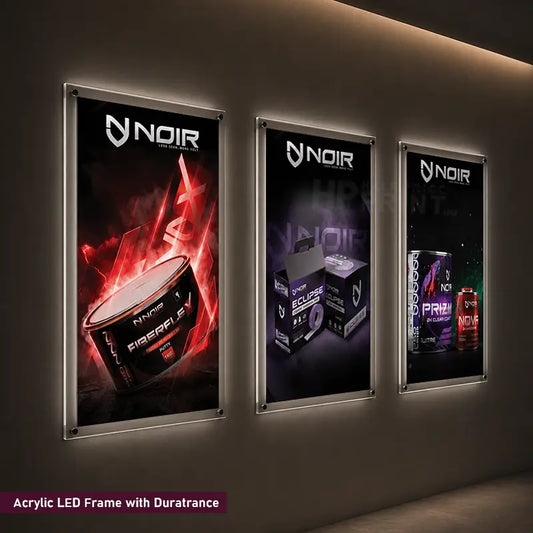 Three vertically oriented acrylic LED frame wall art displays mounted on a dark wall, each showing different branded product posters. The left panel glows red, the center panel is dark purple, and the right panel is dark with neon accents.