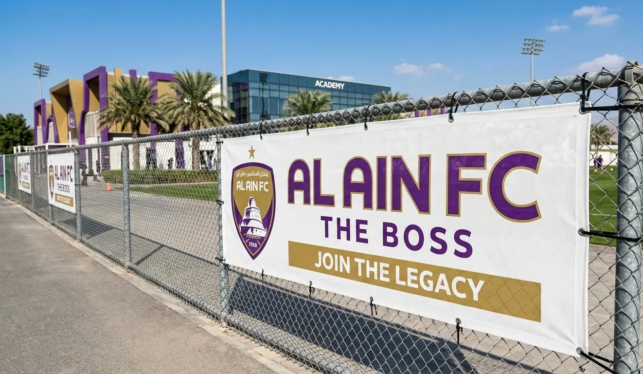 Alain FC banner on a chain-link fence with sports facility in the background