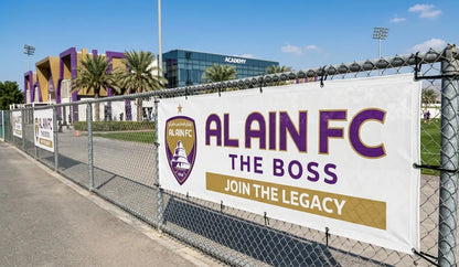 Alain FC banner on a chain-link fence with sports facility in the background