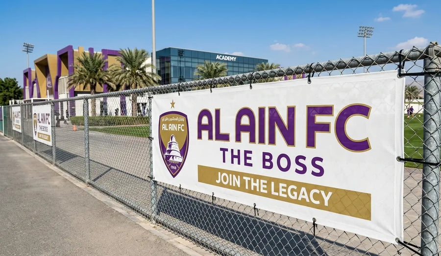 Alain FC banner on a chain-link fence with sports facility in the background