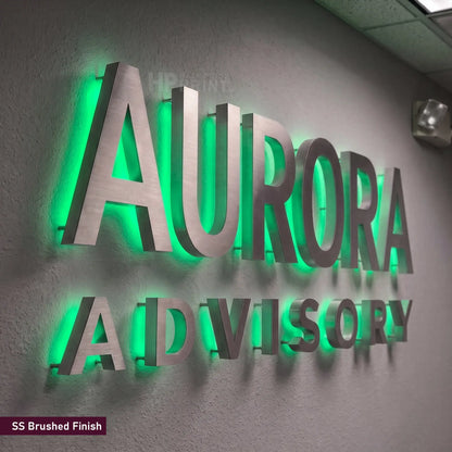 3D metal wall sign with brushed silver lettering reading 'AURORA ADVISORY' backlit with bright green LED glow, mounted on a textured gray wall.