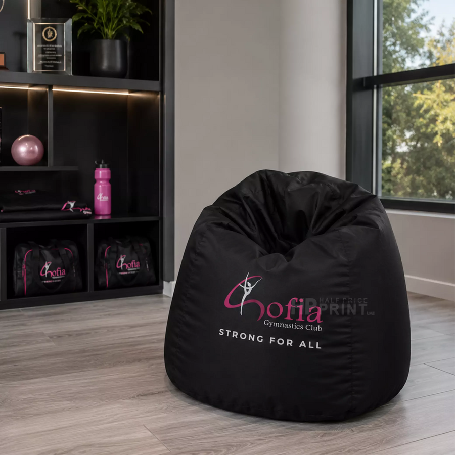 Black bean bag chair with 'Gofia Gymnastics Club' branding in a room with shelves and window.