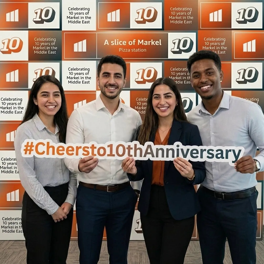 Four people holding a sign with '#Cheersto10thAnniversary' in front of a branded wall.