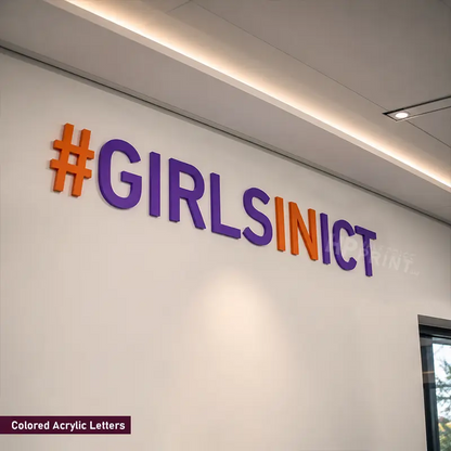 Acrylic wall letters spelling '#GIRLSINICT' in purple and orange, mounted on a white wall in an indoor setting.