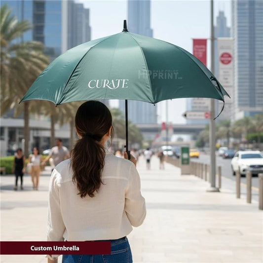 Person holding a green umbrella with 'Curate' branding on a city street.