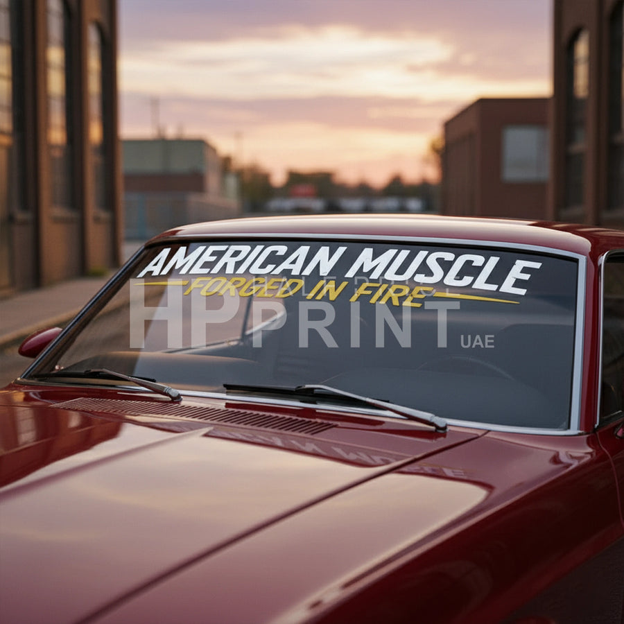 Car with 'American Muscle' decal on the windshield against a sunset cityscape.