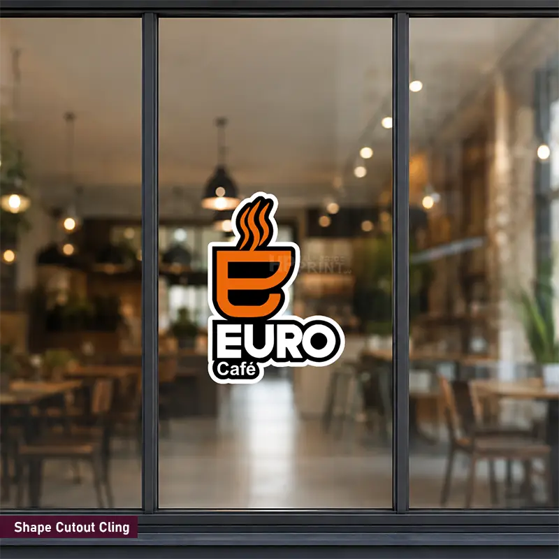 A shape-cut vinyl wall cling featuring the 'EURO Café' logo, shown applied to a window in a blurred cafe interior. The decal has an orange coffee cup icon with steam, white text, and a black outline.