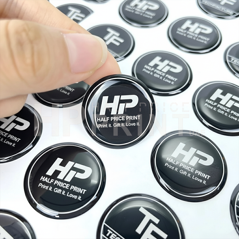 Hand holding a Half Price Print epoxy sticker among multiple similar stickers.