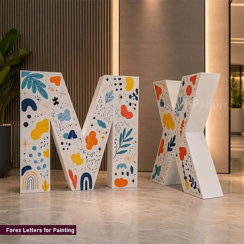 Four freestanding decorative forex letters M, X, and two additional letters with colorful abstract floral and leaf patterns on a white base, displayed indoors on a polished floor against a modern interior wall.