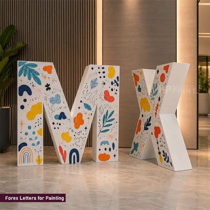Four freestanding decorative forex letters M, X, and two additional letters with colorful abstract floral and leaf patterns on a white base, displayed indoors on a polished floor against a modern interior wall.