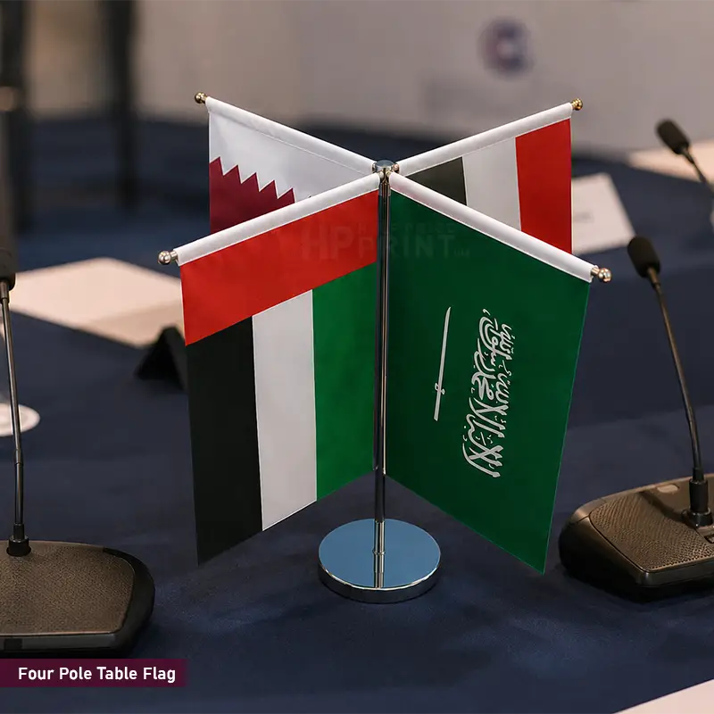 Four pole table flags displaying the national flags of Bahrain, Qatar, Kuwait, and Saudi Arabia, arranged on a dark blue table with microphones in the background.