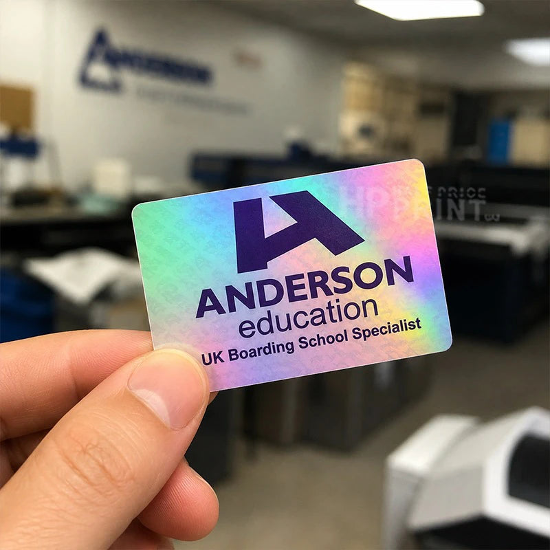 A hand holding a holographic business card for Anderson Education, UK Boarding School Specialist, with the company logo and name printed on it. The background shows a blurred office environment with the Anderson Education logo on the wall.
