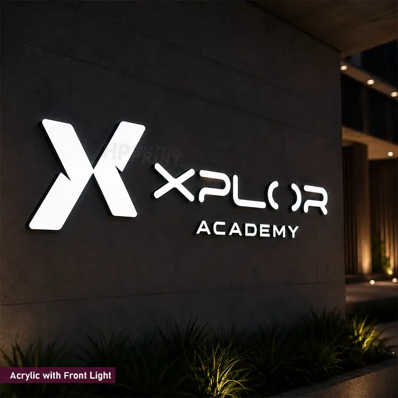 A large illuminated acrylic sign reading 'XPLOR ACADEMY' with a stylized X logo, mounted on a dark building wall at night. The sign is bright white with front-facing lighting, with small plants along the bottom and a faint watermark across the center.