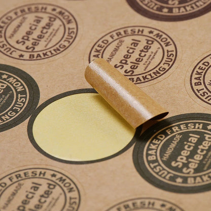 Custom round brown kraft paper stickers with text on them, displayed on a table.