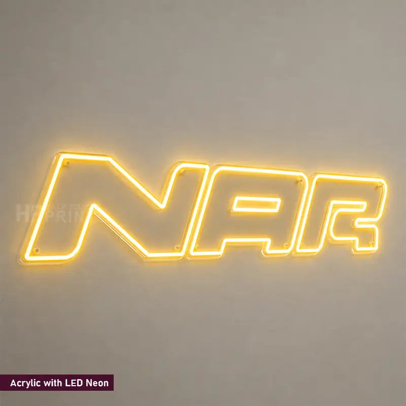 A glowing LED neon-style sign spelling 'NAR' in a warm yellow light, mounted against a plain light gray wall. Small text in the lower-left corner reads 'Acrylic with LED Neon'.