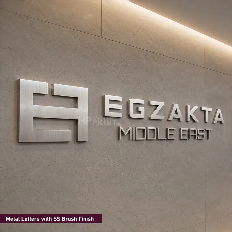 3D metal sign letters with a brushed silver finish mounted on a textured beige wall, featuring the brand name 'EGZAKTA MIDDLE EAST' alongside a stylized logo.