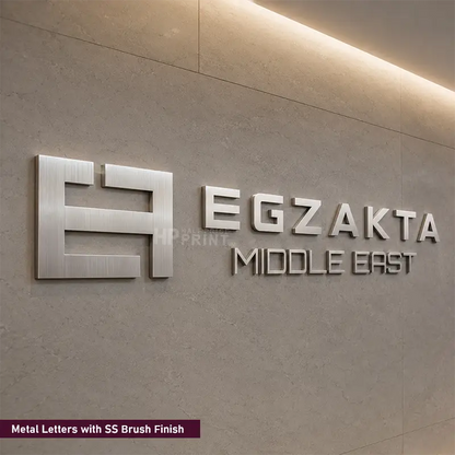 3D metal sign letters with a brushed silver finish mounted on a textured beige wall, featuring the brand name 'EGZAKTA MIDDLE EAST' alongside a stylized logo.