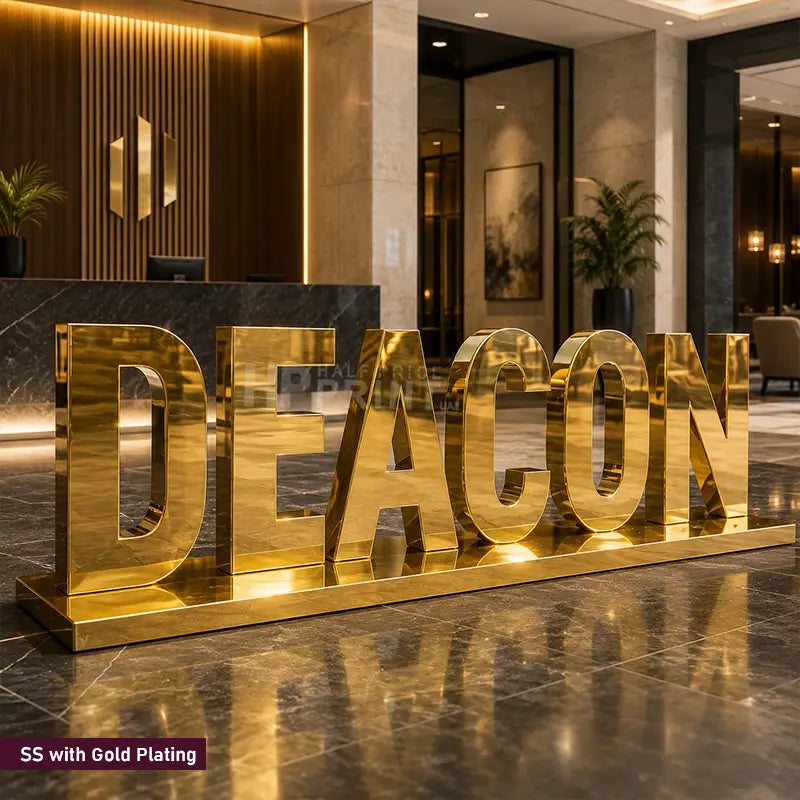 Large gold-plated freestanding letters spelling DEACON placed in a modern lobby or reception area, with polished marble flooring and warm interior lighting in the background.