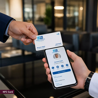 A close-up of a hand holding a white NFC card above a smartphone displaying the matching digital profile, with a blurred office background.
