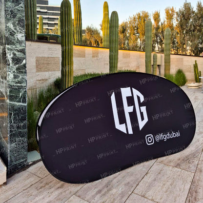 Black oval sign with 'LFG' and social media handle on a stone surface with cacti in the background