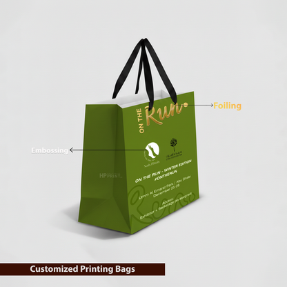 Green paper gift bag with gold text and black handles on a light gray background