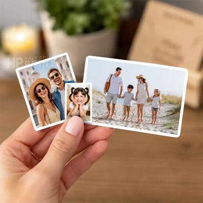 A hand holds two small, printed photo cards sticker with rounded corners in front of a blurred indoor background. One card shows a couple, and the other shows a family of four walking on a beach.