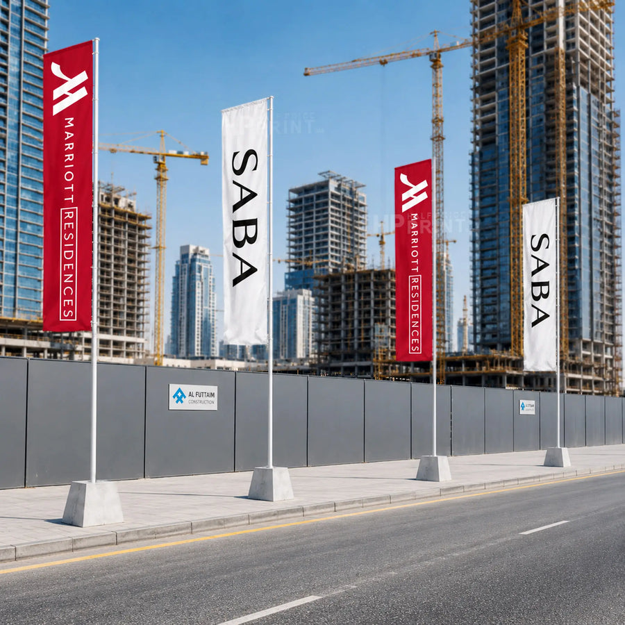 Three vertical Marriott Residences flag banners are displayed on a construction site. Two banners are red with white Marriott Residences branding, and one banner is white with black SABA branding.