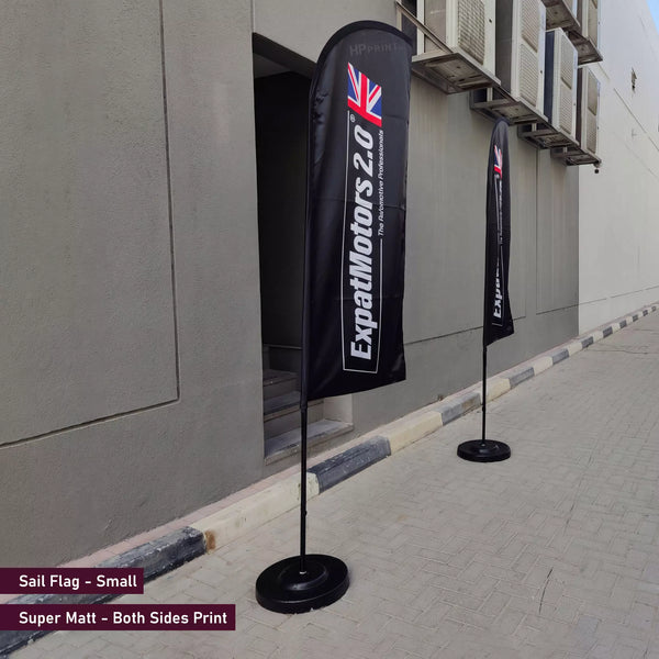 Two black flags with branding on a sidewalk next to a building.