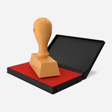 Wooden stamp resting on a red ink pad inside an open black case.
