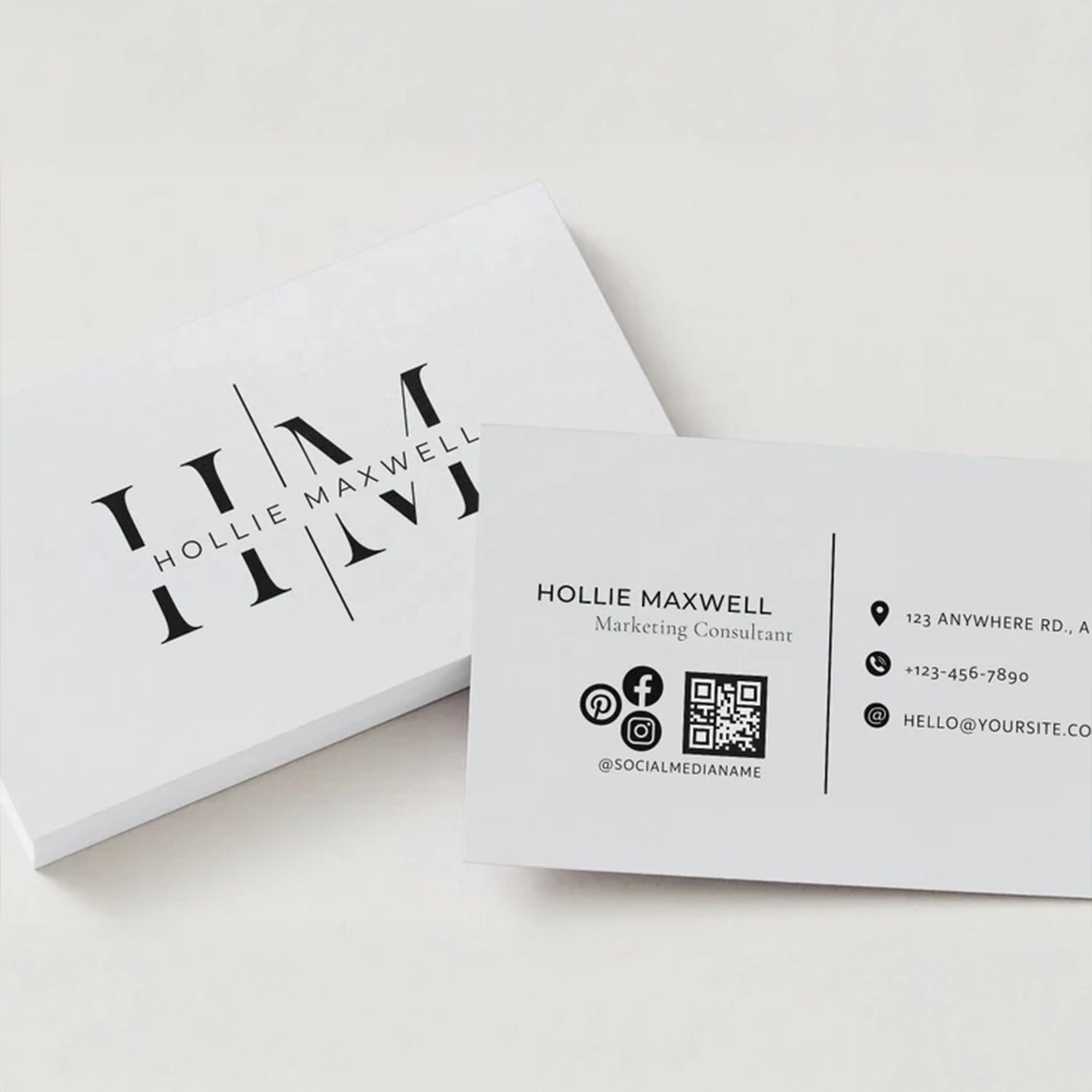 Minimalist white business cards with black typography, featuring the name “Hollie Maxwell” and a clean logo design, neatly stacked on a light background.
