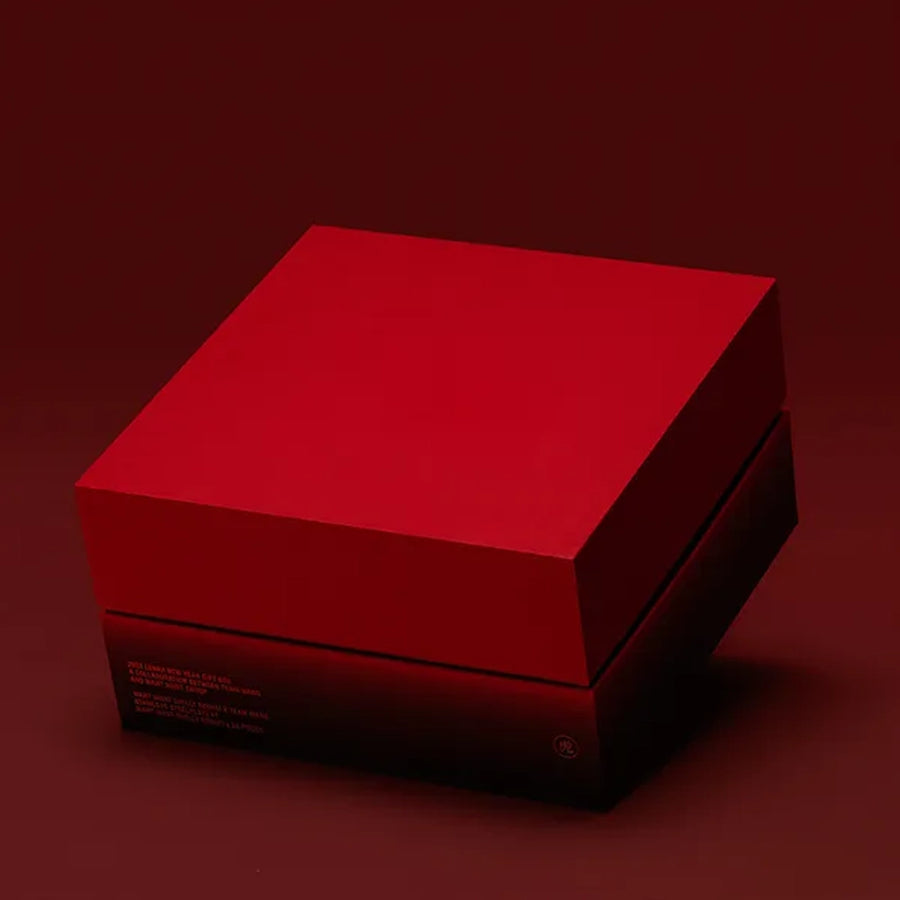 A matte red square gift box with a fitted lid sits on a dark red surface, shown from a slight angle with soft shadows creating a clean, minimalist look.