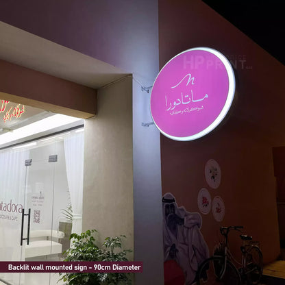 Backlit wall-mounted sign with a purple circle on a Dubai building exterior