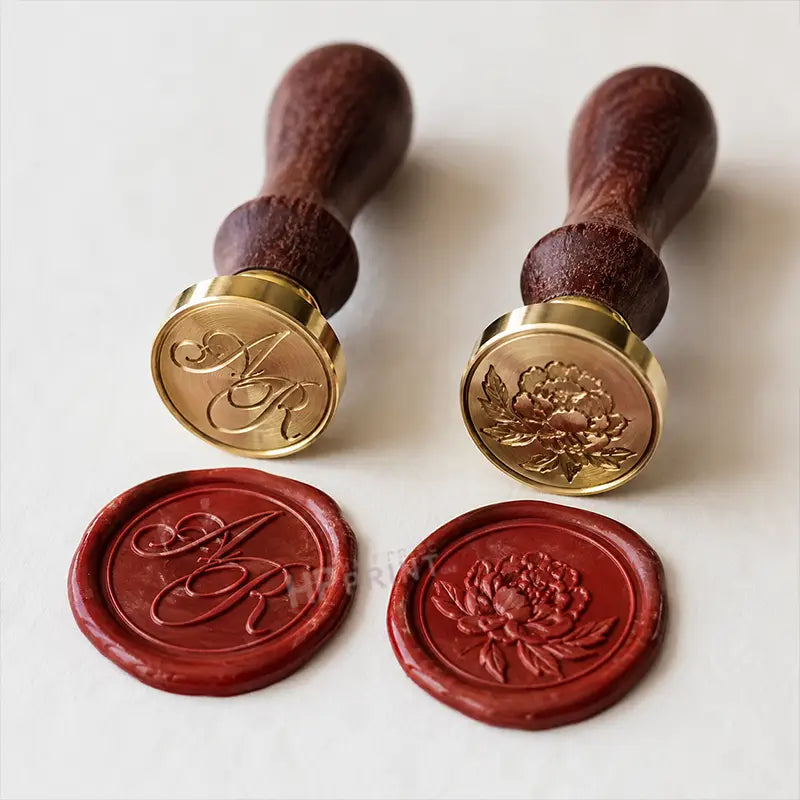 Two wooden-handled wax seals with gold-toned metal stamp heads, shown with two red wax seals below on a light neutral background.