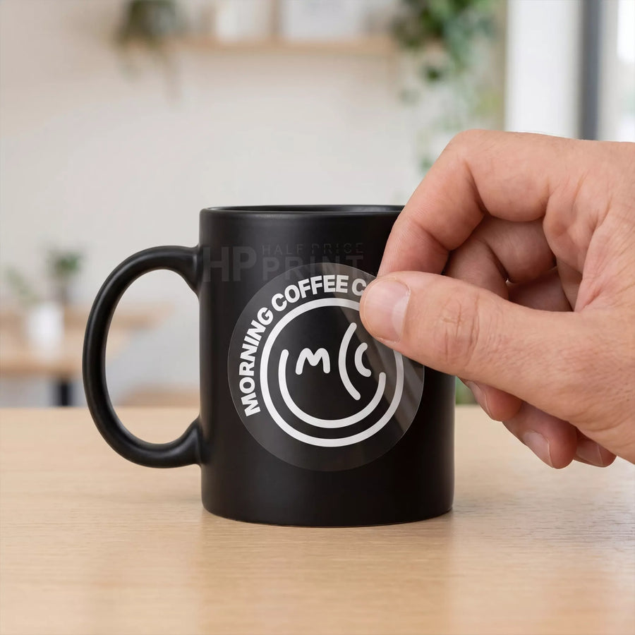 Black mug with a logo and text held by a hand on a wooden surface
