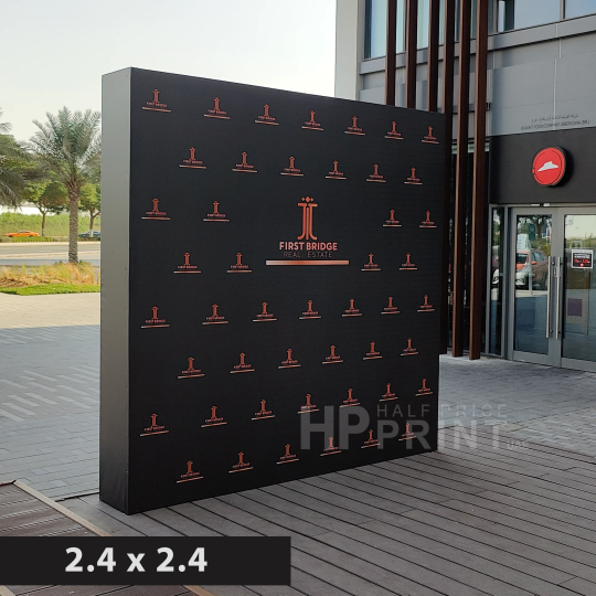 Black step and repeat banner with branding on a wooden deck outside a building.
