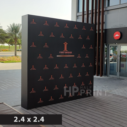 Black step and repeat banner with branding on a wooden deck outside a building.