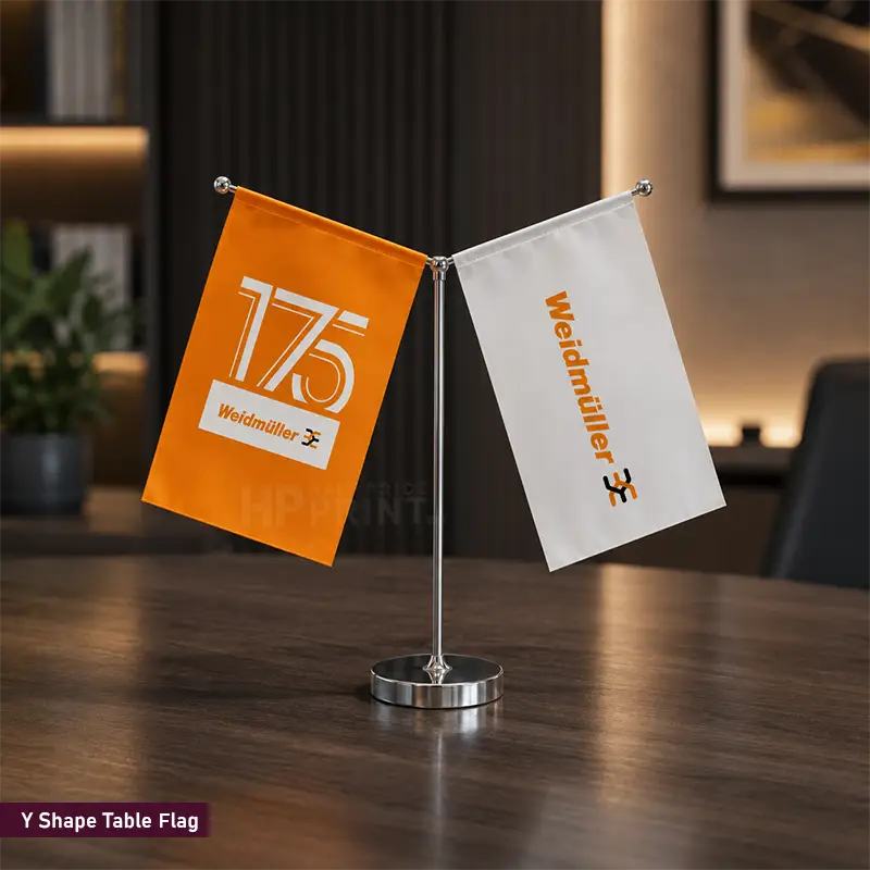 A Y-shaped table flag set on a dark wooden table, featuring one orange flag with '175' and 'Weldmiller' text, and one white flag with 'Weldmiller' text and logo.